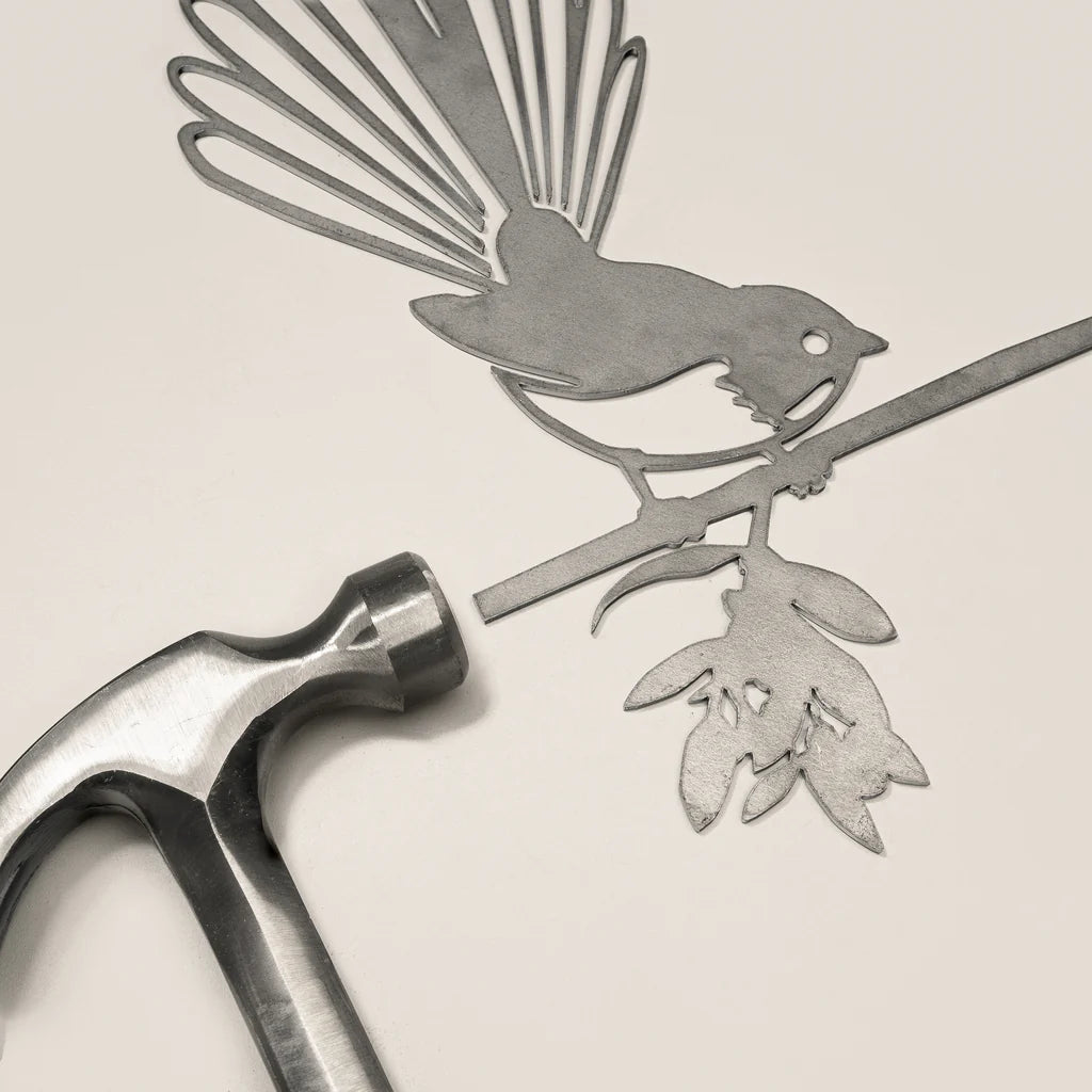 Metal cutout of a bird and branch with a hammer on a beige background