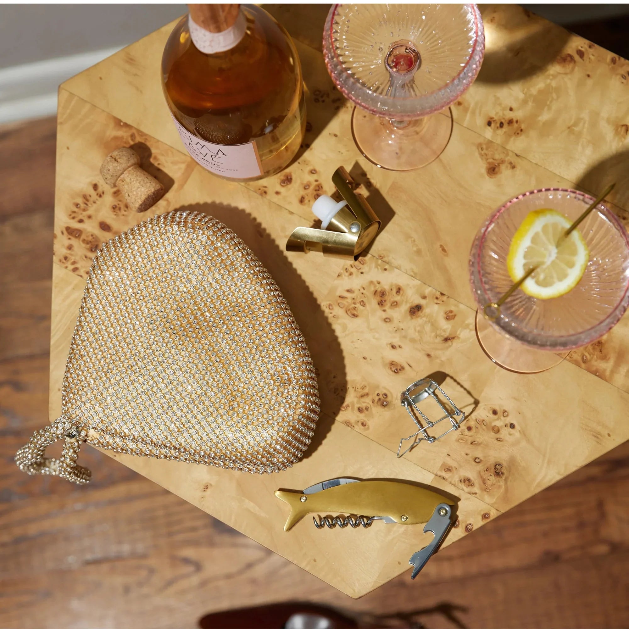 Gold mesh handbag, bottle, and glasses on a wooden table