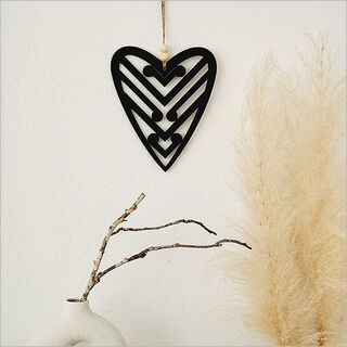 Black heart-shaped decorative item hanging on a white wall with pampas grass and branches.