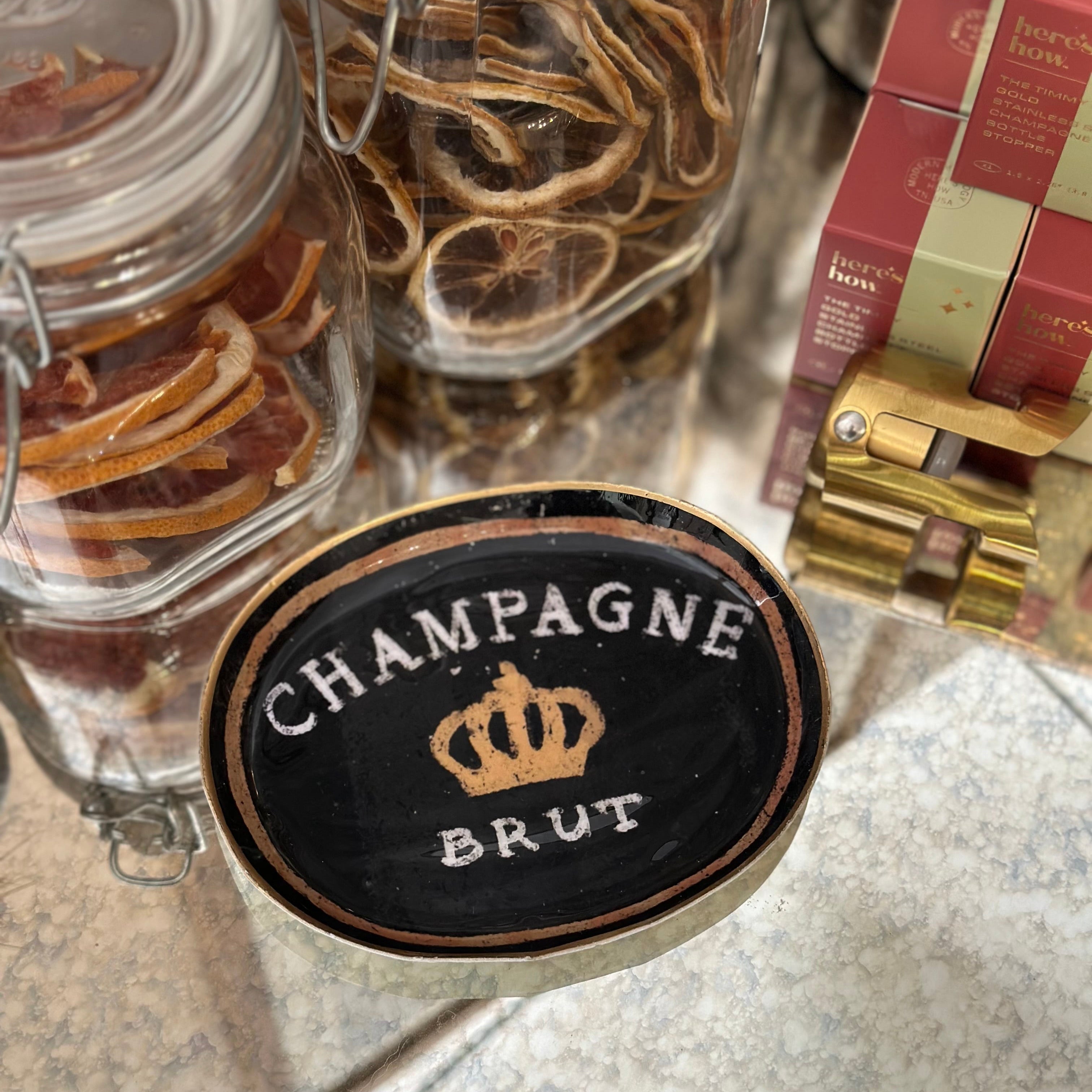 Two jars with dried fruits and a decorative dish labeled 'Champagne Brut' on a marble surface.