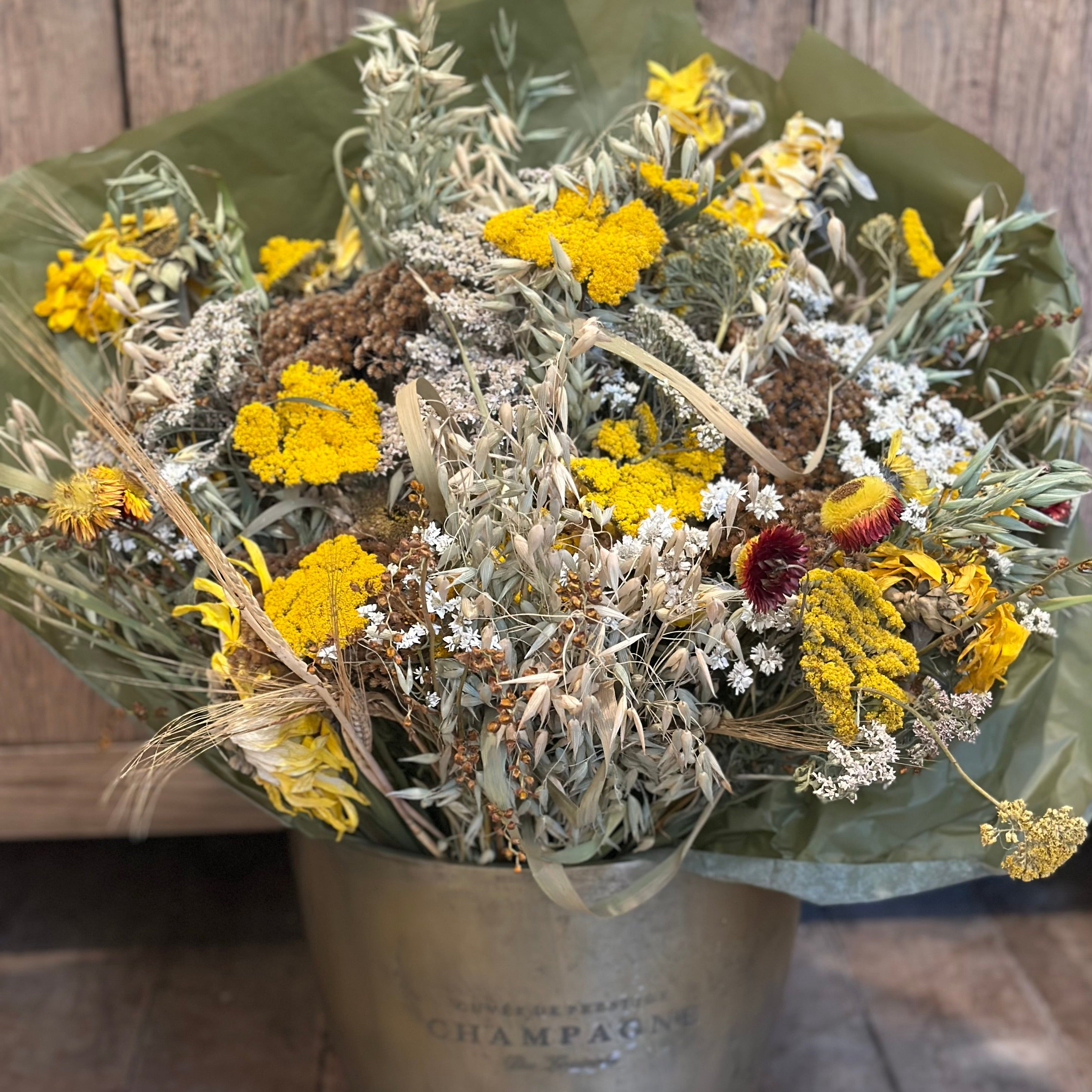 Bouquet of dried flowers in a metal container on a wooden floor.
