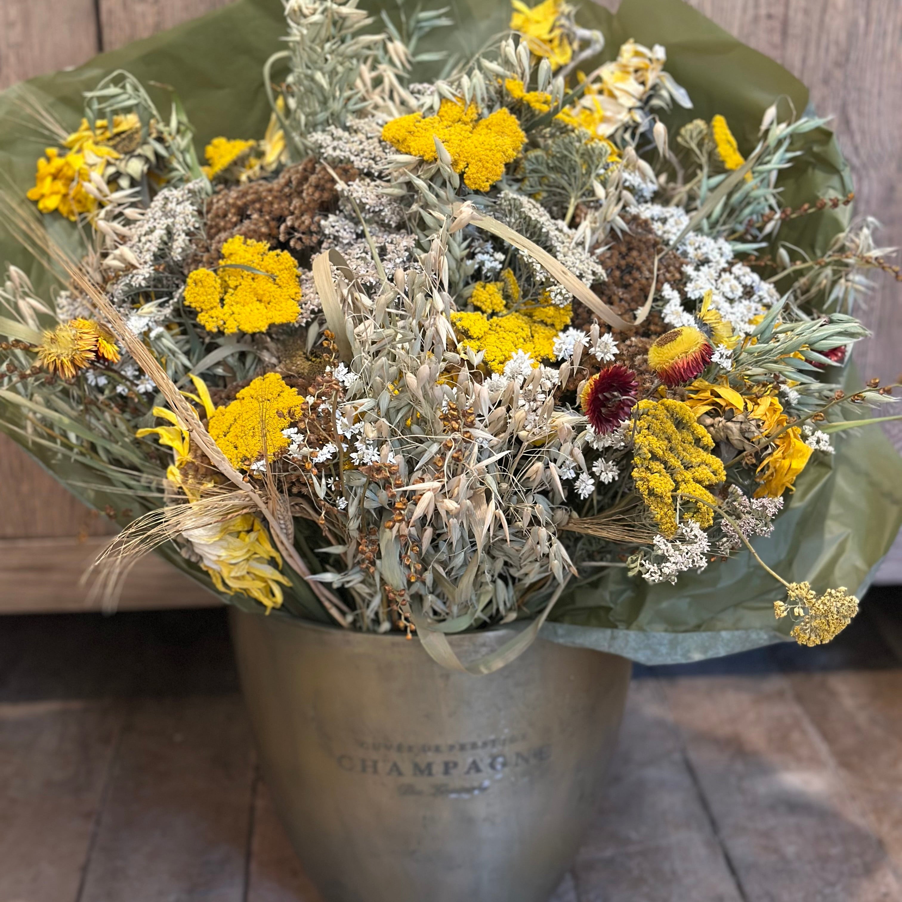 Bouquet of dried flowers in a metal container on a wooden floor.