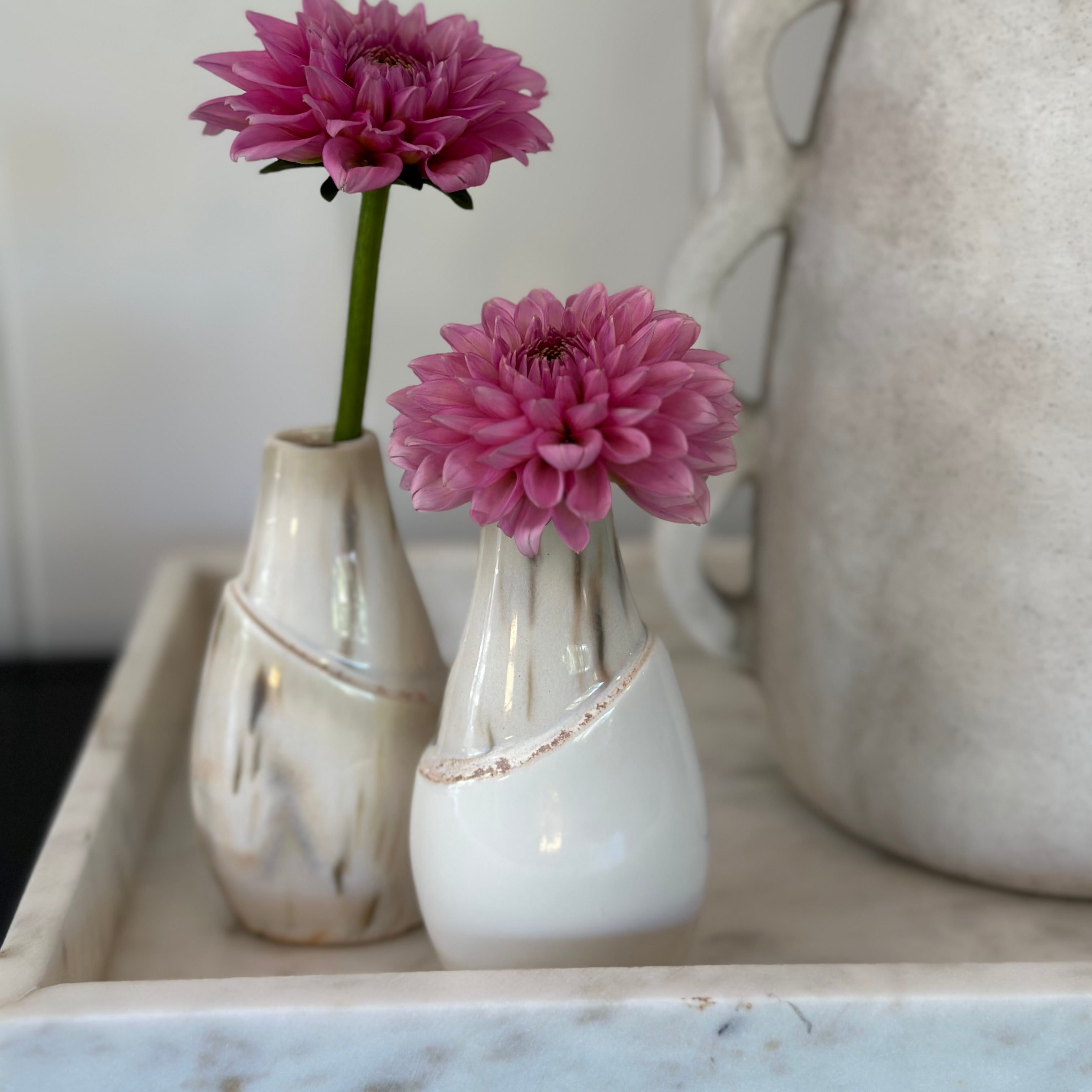 Two small ceramic vases with pink flowers on a marble surface.