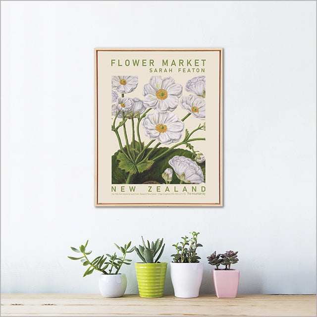 Framed floral poster titled 'Flower Market' by Sarah Featon on a wall with potted plants below.