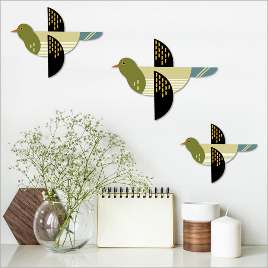Decorative wall birds on a white wall with a vase, notebook, and candle in the foreground.