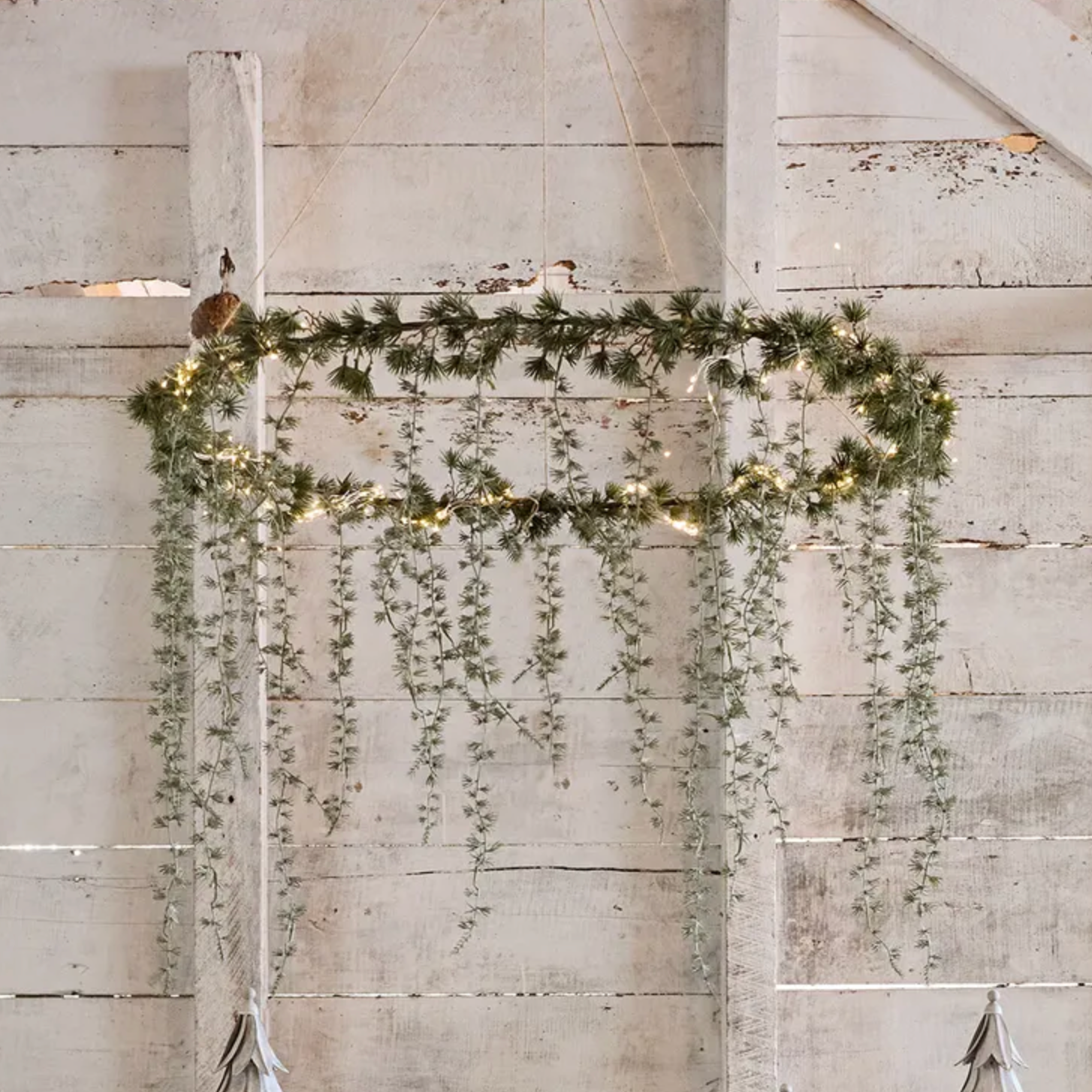 Decorative arch made of greenery with lights against a wooden wall.