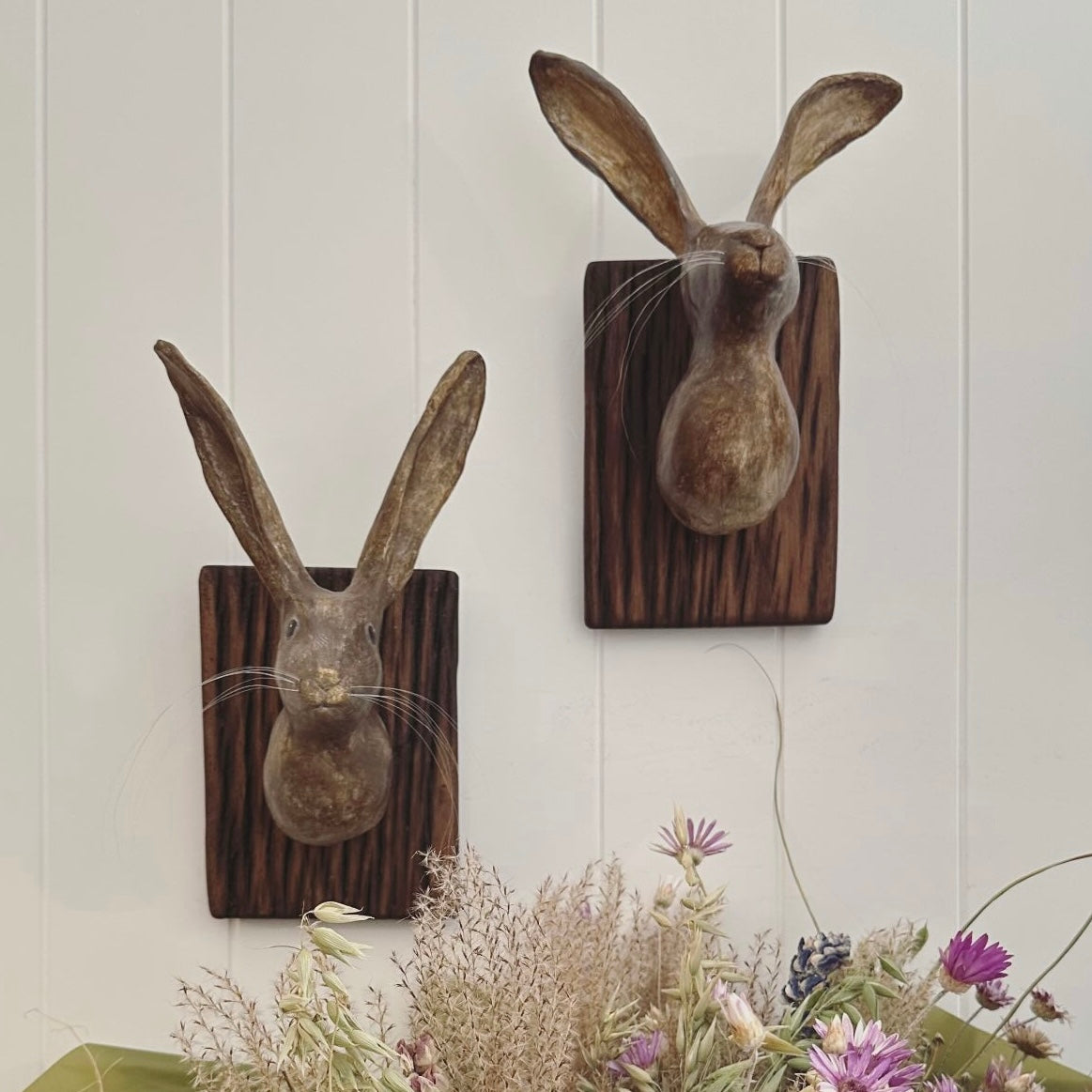 Two rabbit wall decorations on wooden boards with a floral arrangement at the bottom.