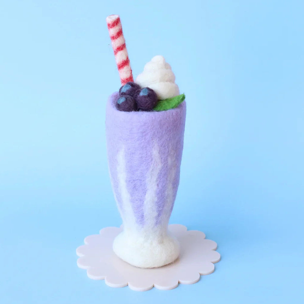 Felted milkshake with whipped cream, berries, and a straw on a blue background