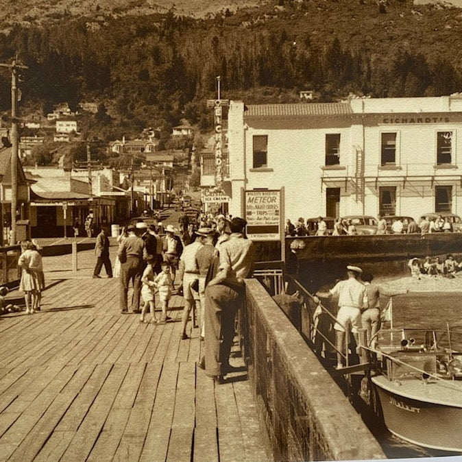 Vintage black and white photo of the Queenstown wharf with people and buildings.