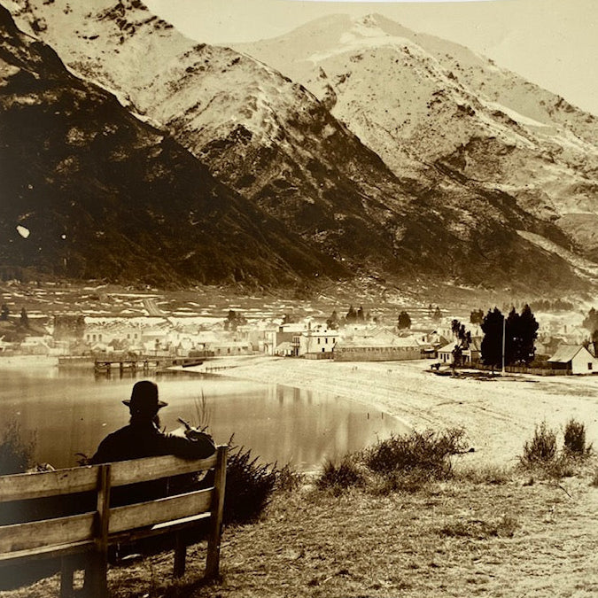 Vintage photograph of a person sitting on a bench overlooking Queenstown bay.