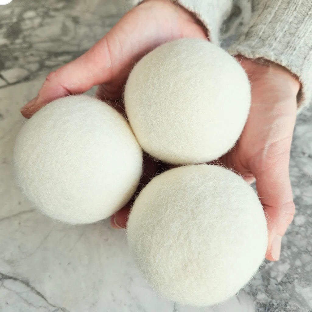 Three white laundry detergent balls held in a hand on a marble surface