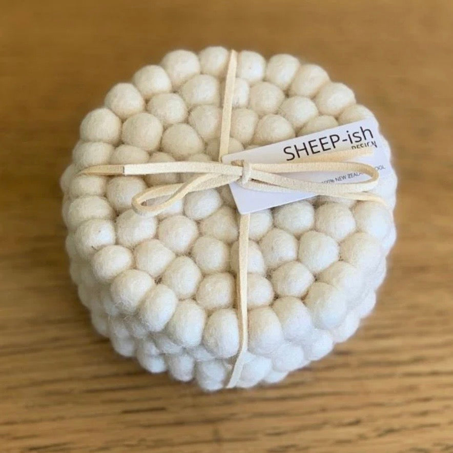 White ball sheepish wool coaster with a bow and 'SHEEP-ish' label on a wooden surface