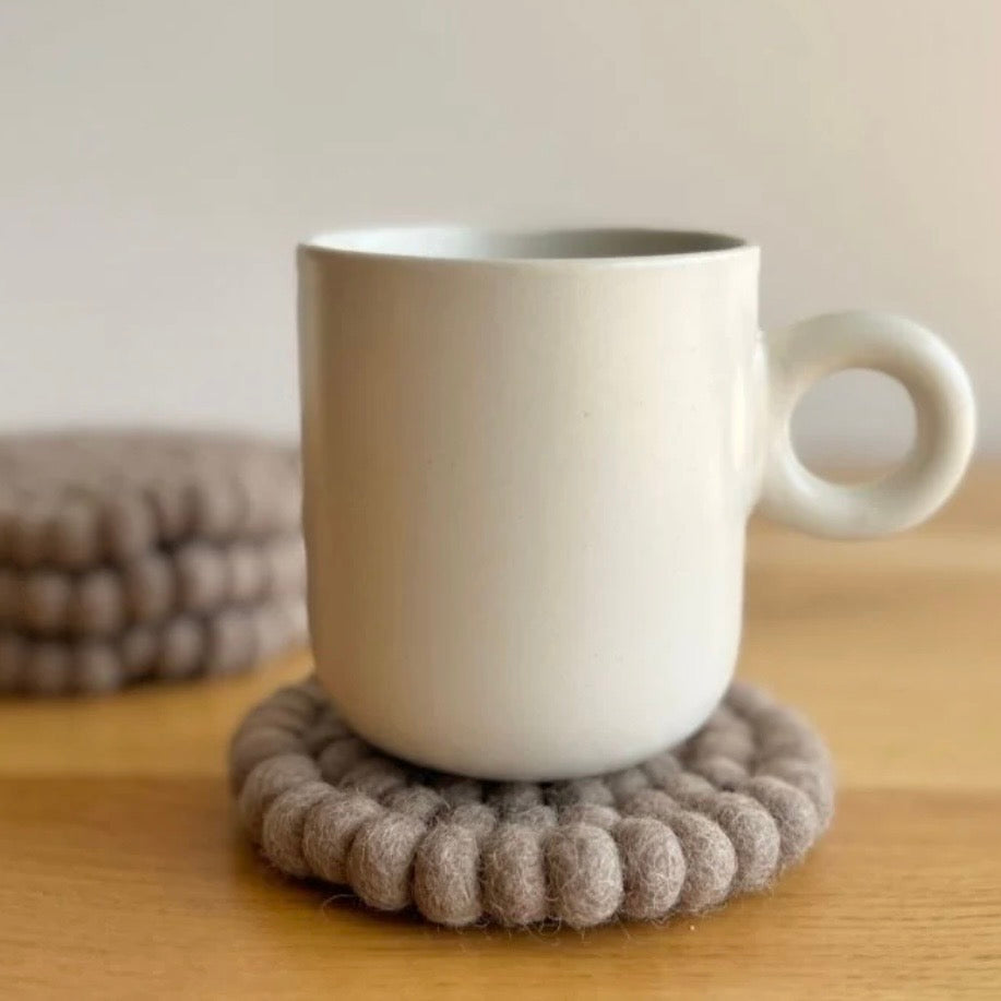 White mug on a textured brown 100% New Zealand wool coaster with a blurred background