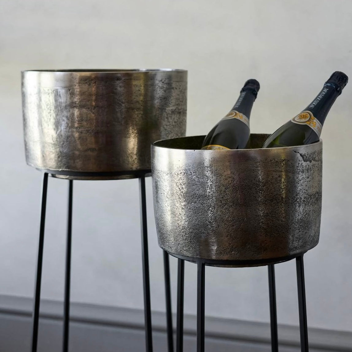 Two metallic ice buckets with bottles of champagne on a plain background