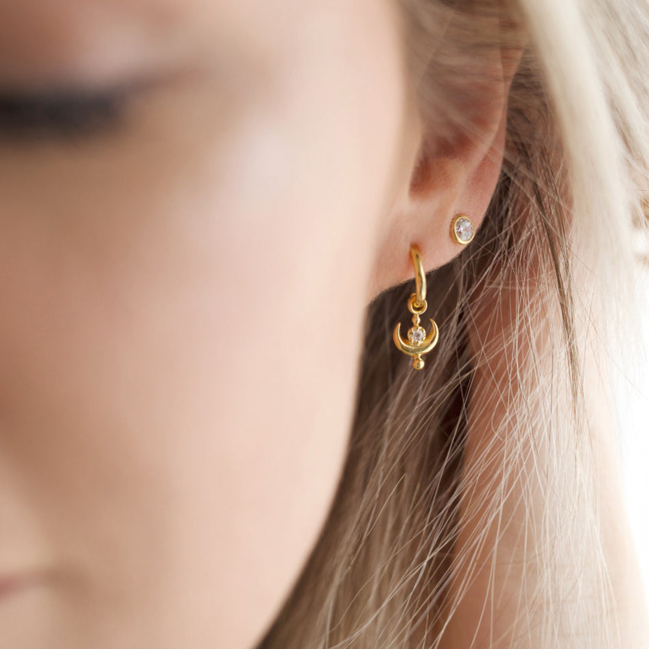 Close-up of a person wearing gold hoop earrings with a blurred background