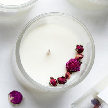 White candles with floral elements on a white surface, surrounded by their packaging.