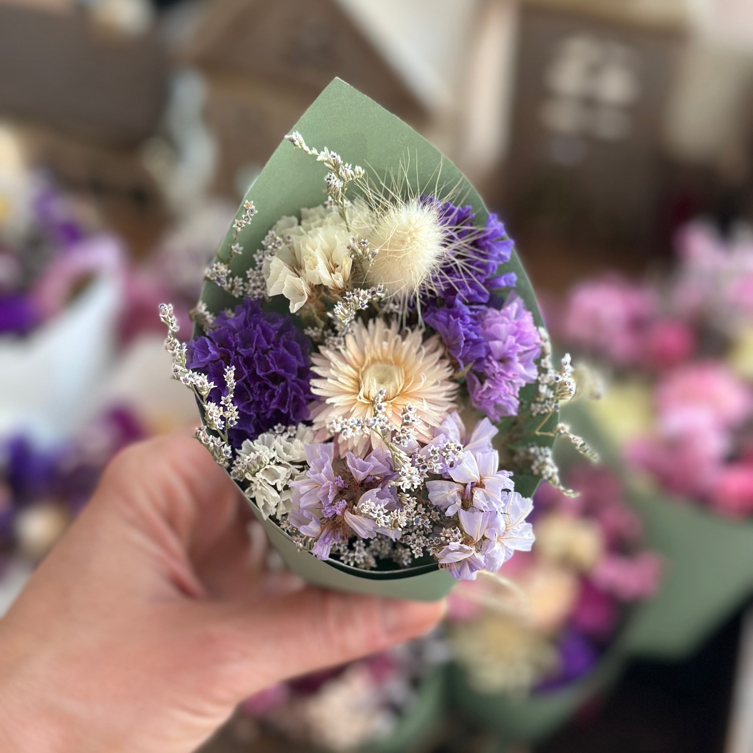 Hand holding a small bouquet of dried flowers with a blurred background