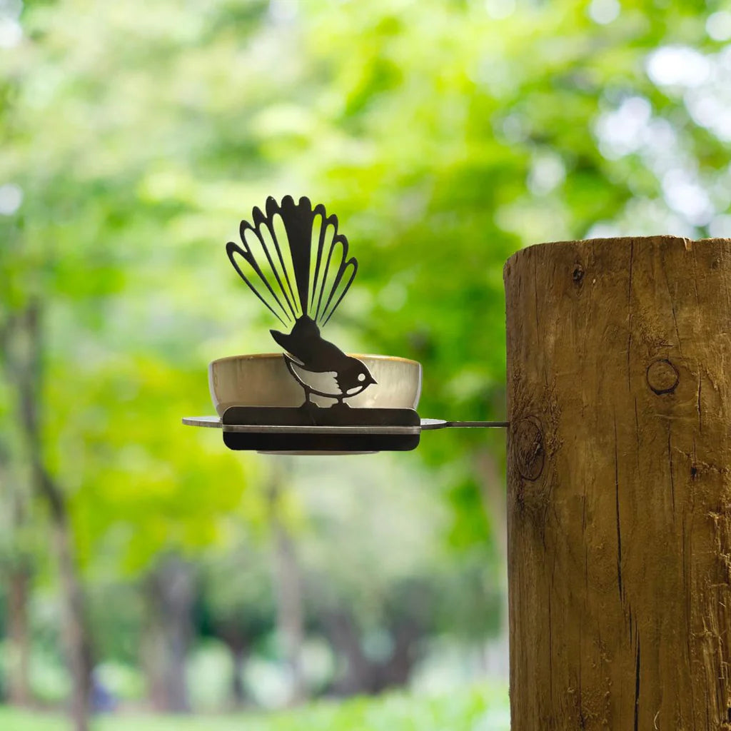 Decorative metal bird sculpture on a wooden post with a blurred green forest background