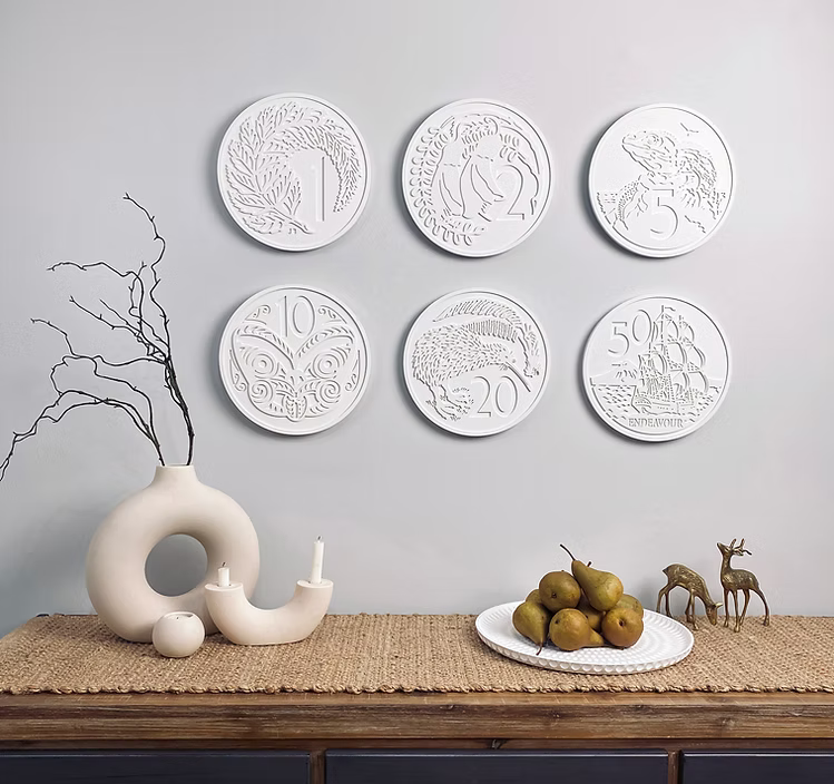 Decorative wall retro new zealand coins embossed designs on a gray wall above a wooden table with a vase, candles, and fruit display.