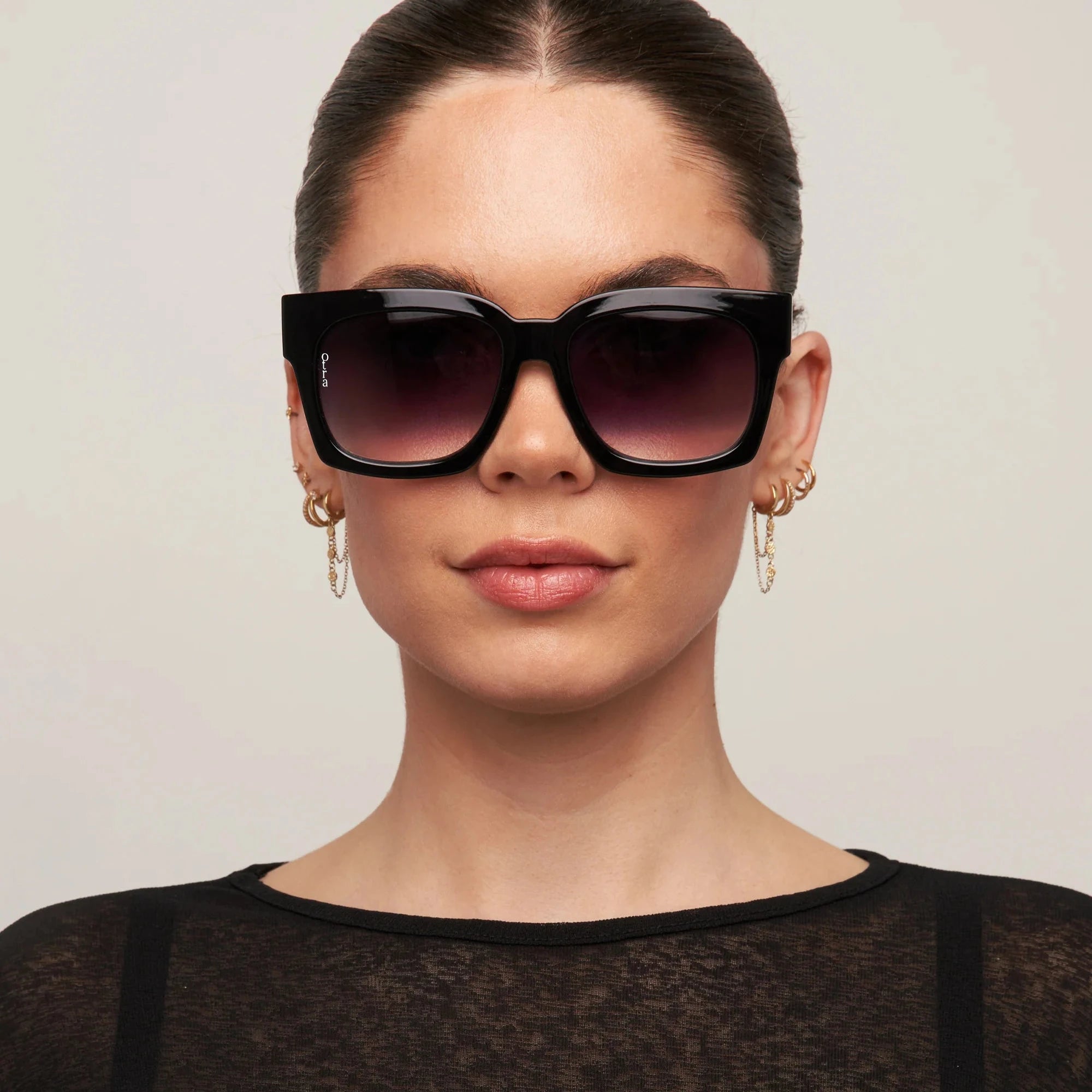 Woman wearing a black outfit and sunglasses against a plain background