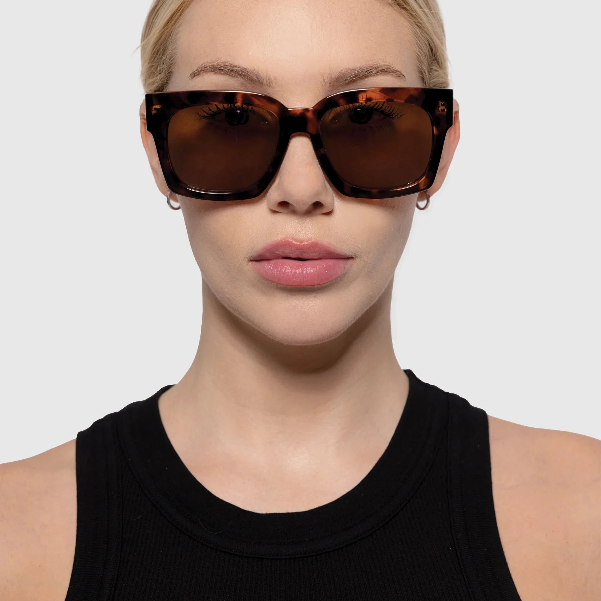 Woman wearing a pair of tortoiseshell sunglasses with a plain background