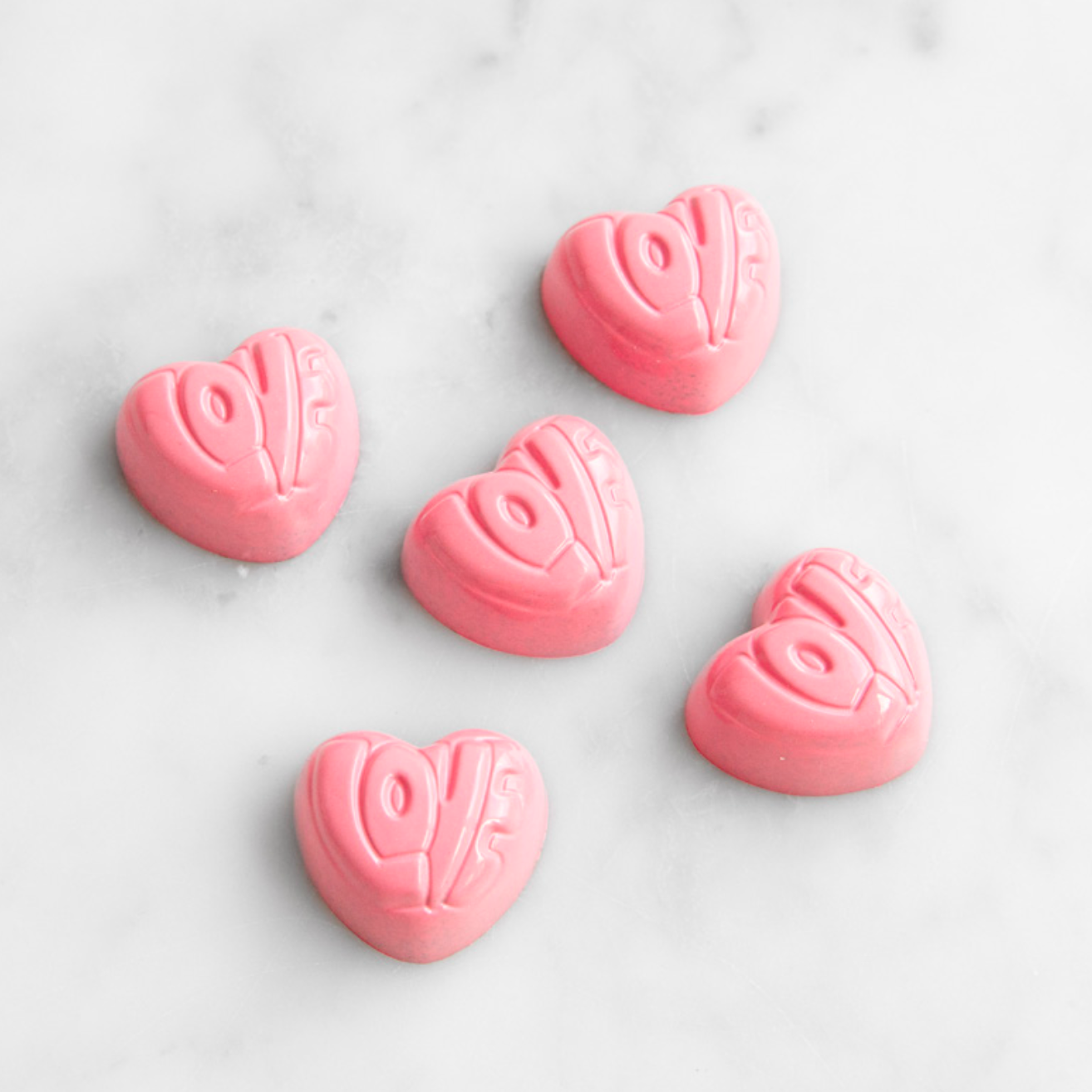 Pink heart-shaped chocolates with designs on a light gray background