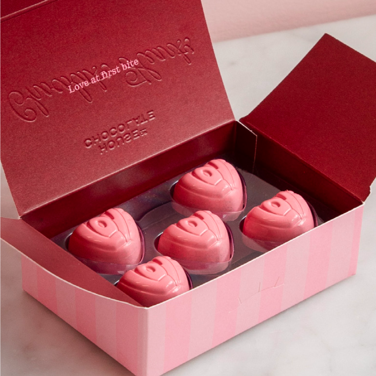 Pink chocolate roses in a Chocolatier Mousen box on a light pink background