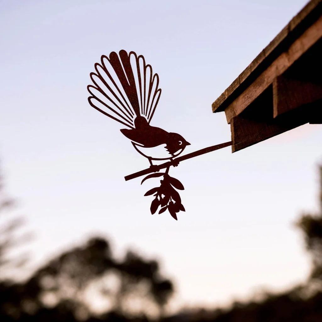 Metal bird fantail sculpture on a branch against a blurred natural background