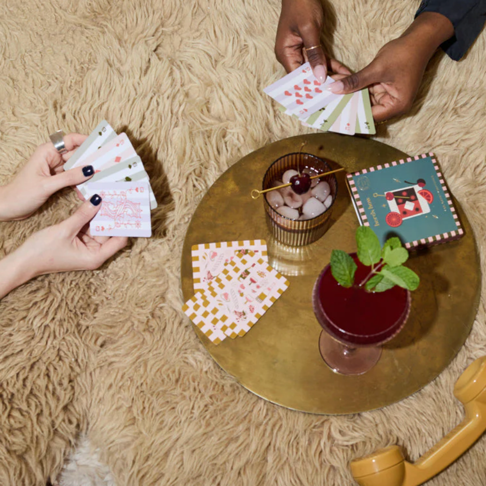 Two people playing cards on a round table with a drink and snacks.