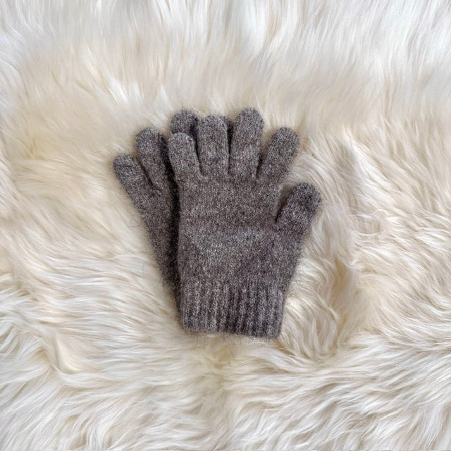 A pair of possum and merino knit gloves in a natural colour laid flat on a white fur surface.