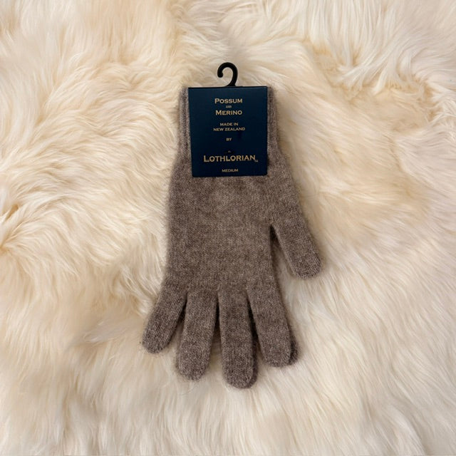 A pair of natural brown possum and merino knit gloves with a black hanger and a dark blue Lothlorian brand tag, displayed on a soft white  fur background.