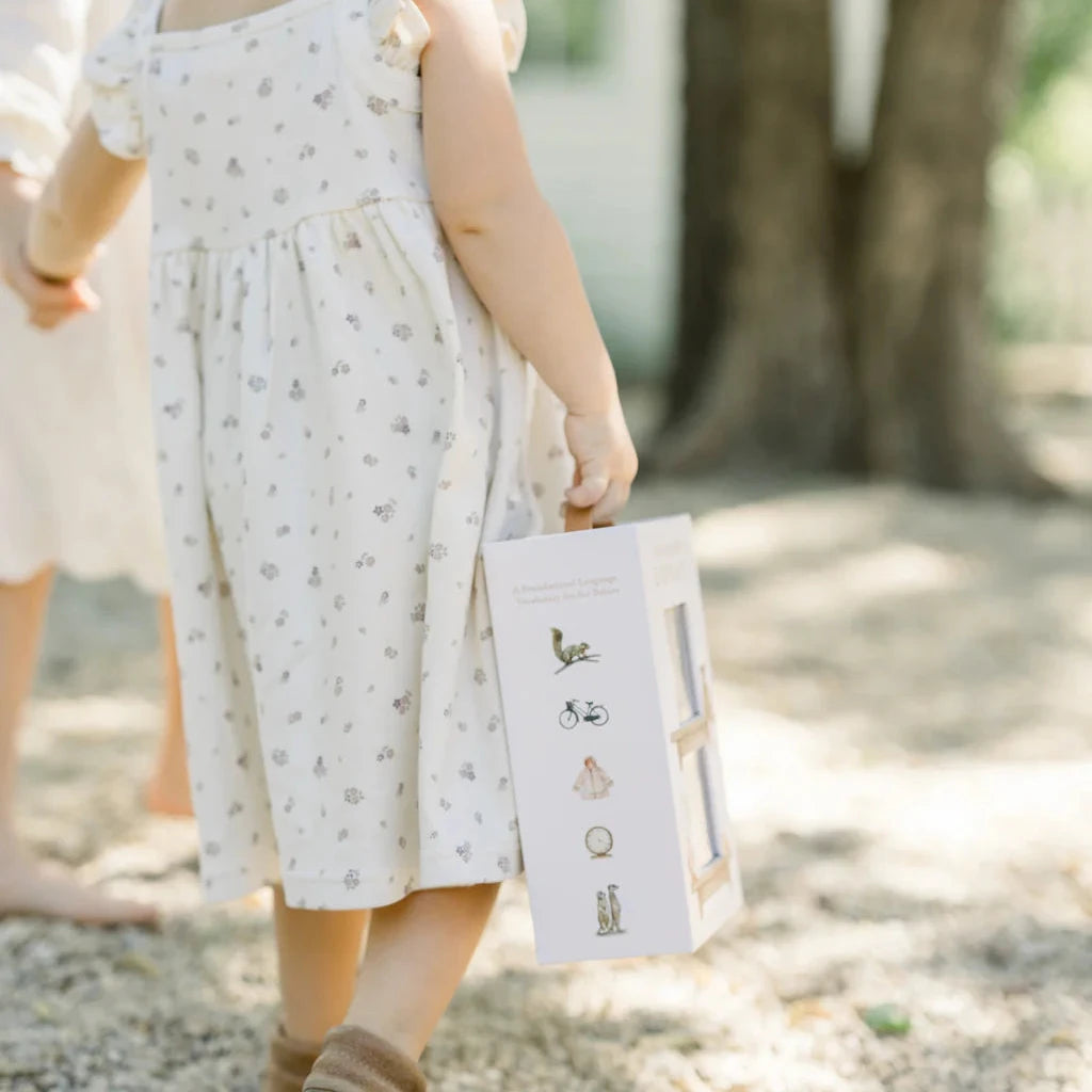 Child in a white dress holding a book outdoors