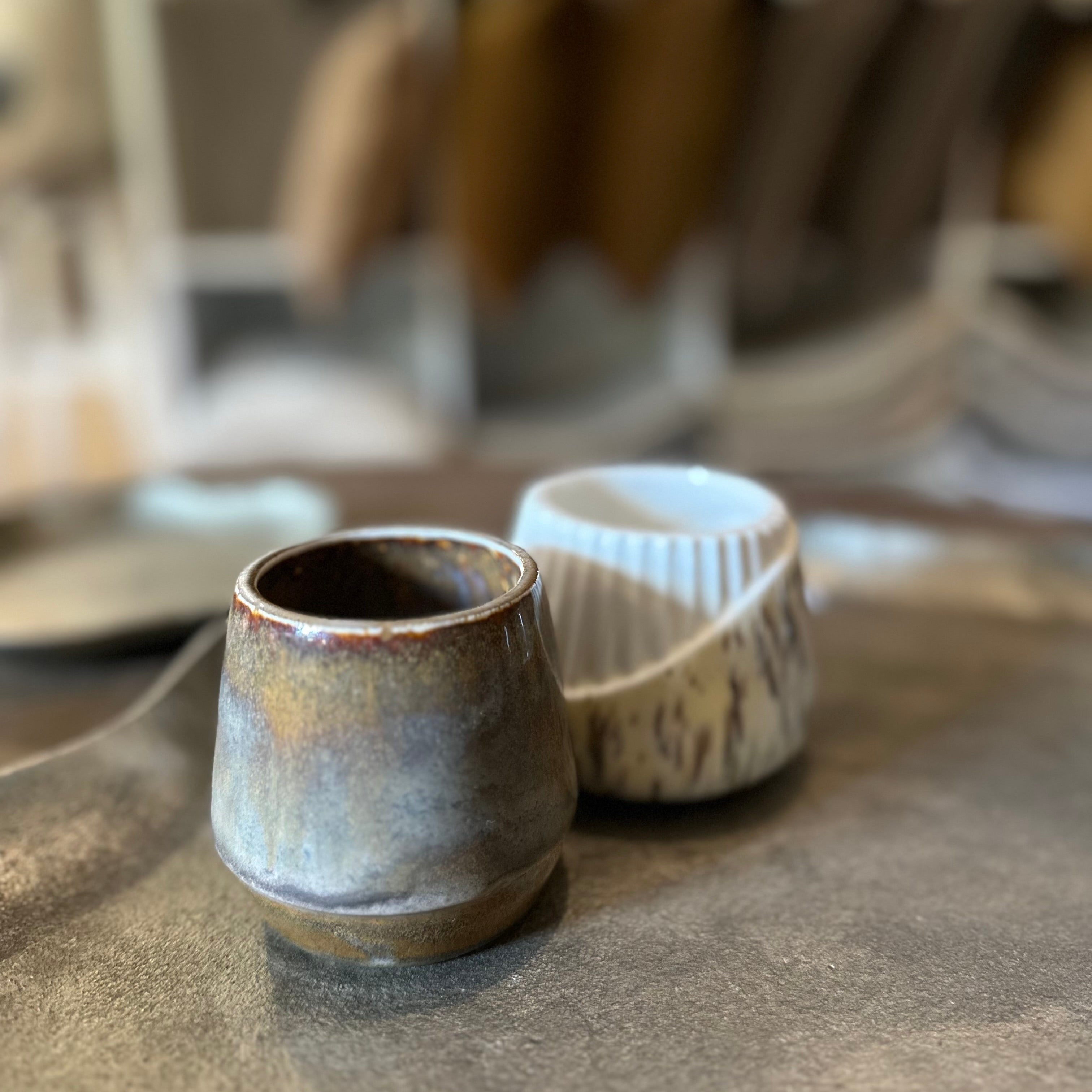 Two ceramic cups on a textured surface with blurred background