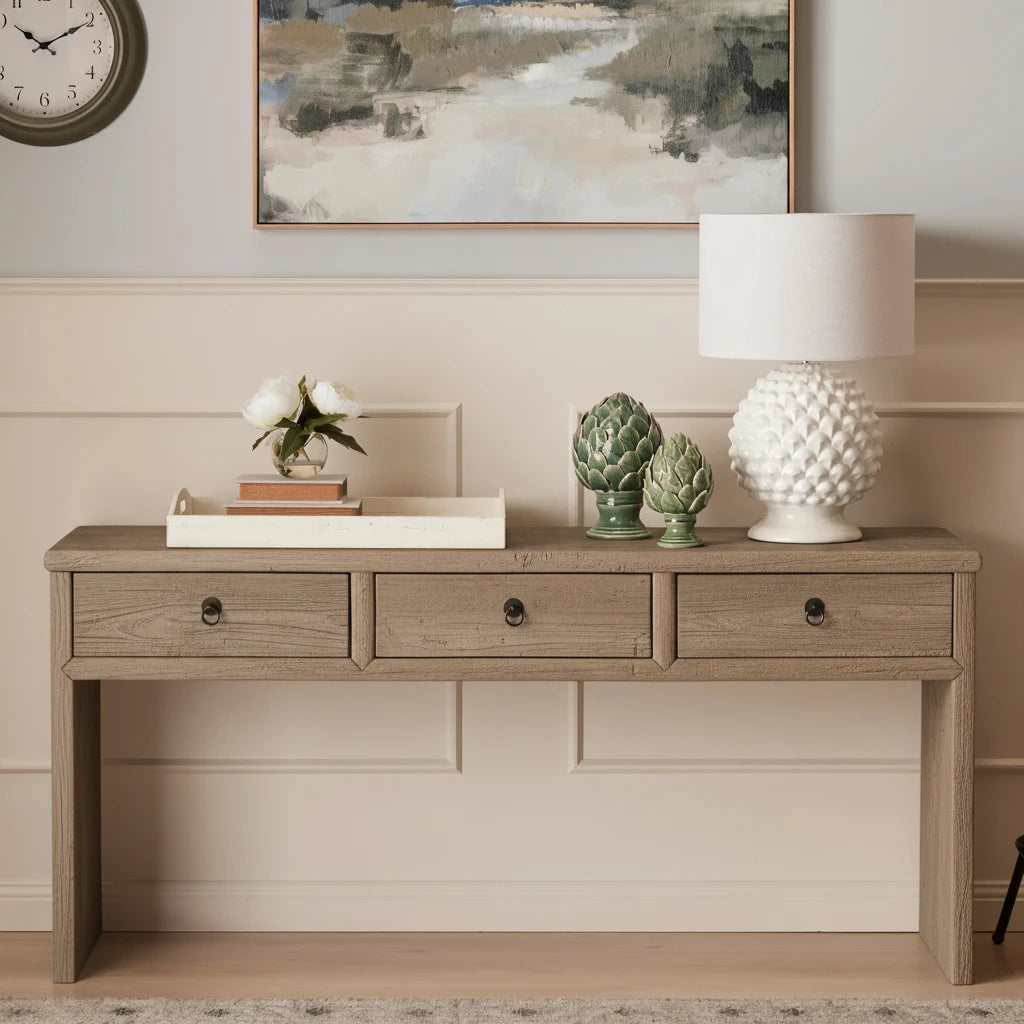 Wooden console table with decorative items against a wall with a clock and painting.