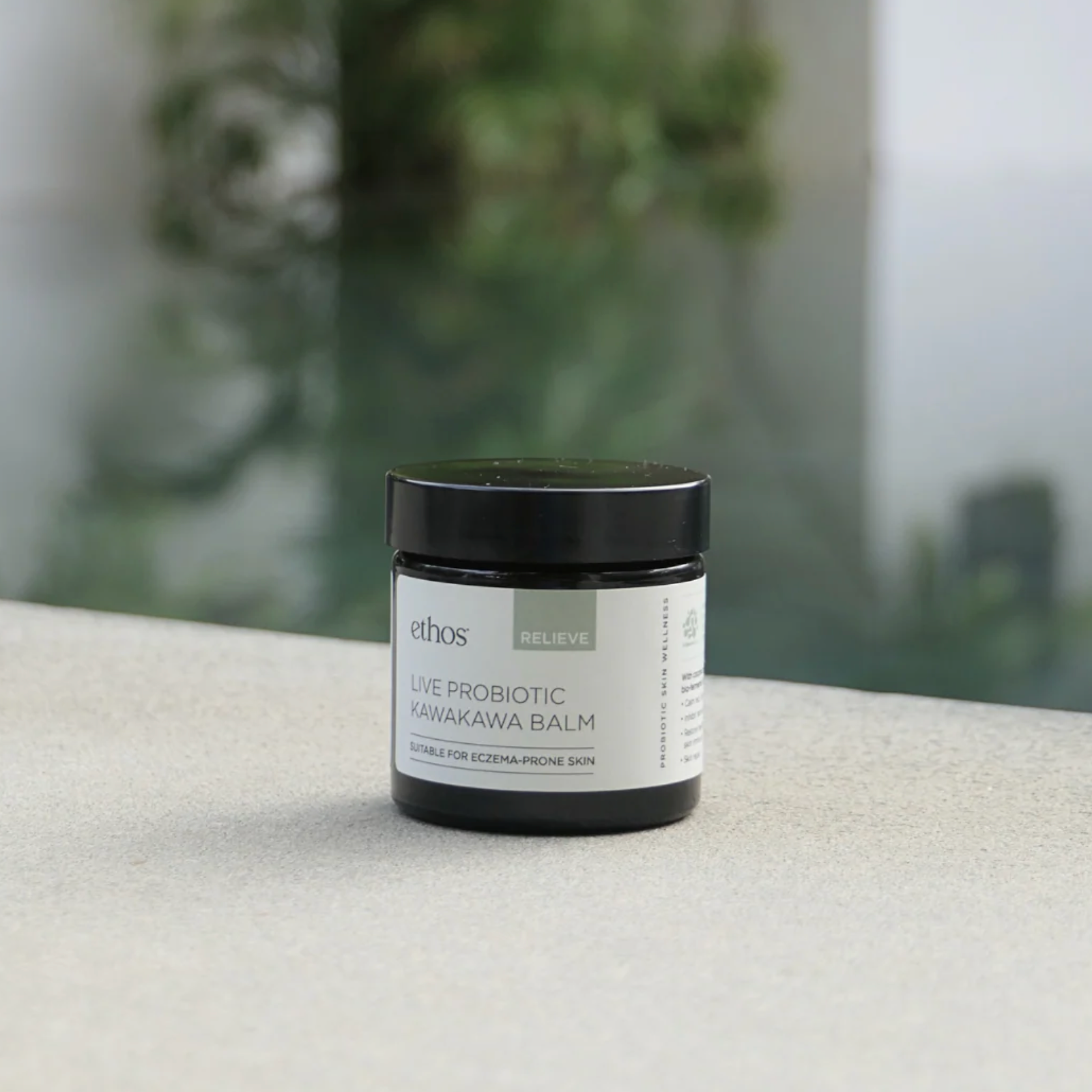 Jar of ethos Live Probiotic Kawakawa Balm on a textured surface with a blurred green background