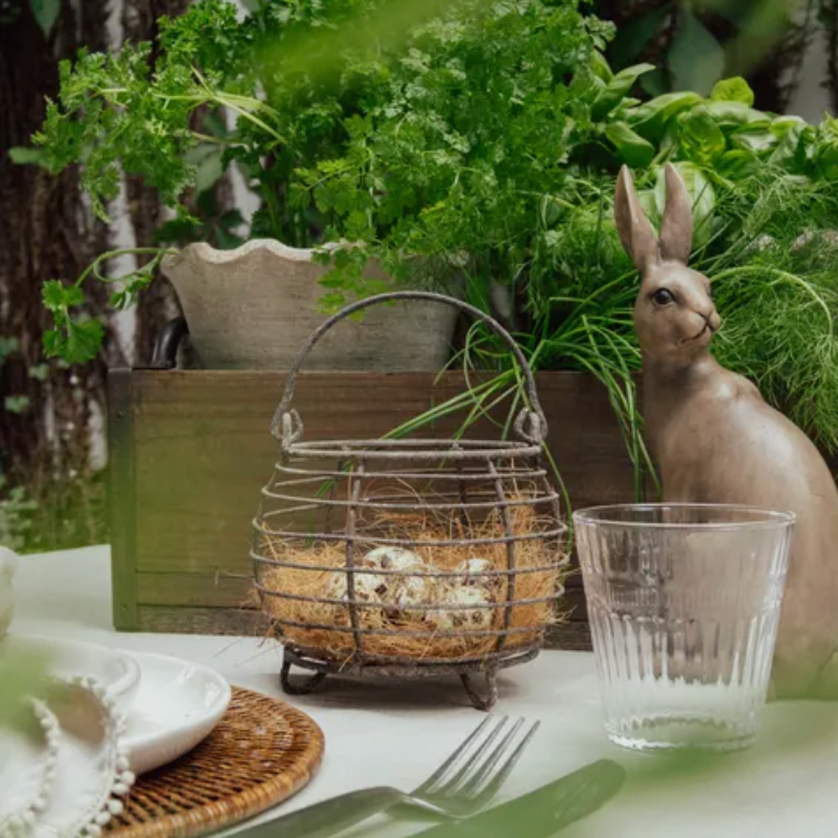 Table setting with a decorative basket, glass, and rabbit figurine in a natural setting.