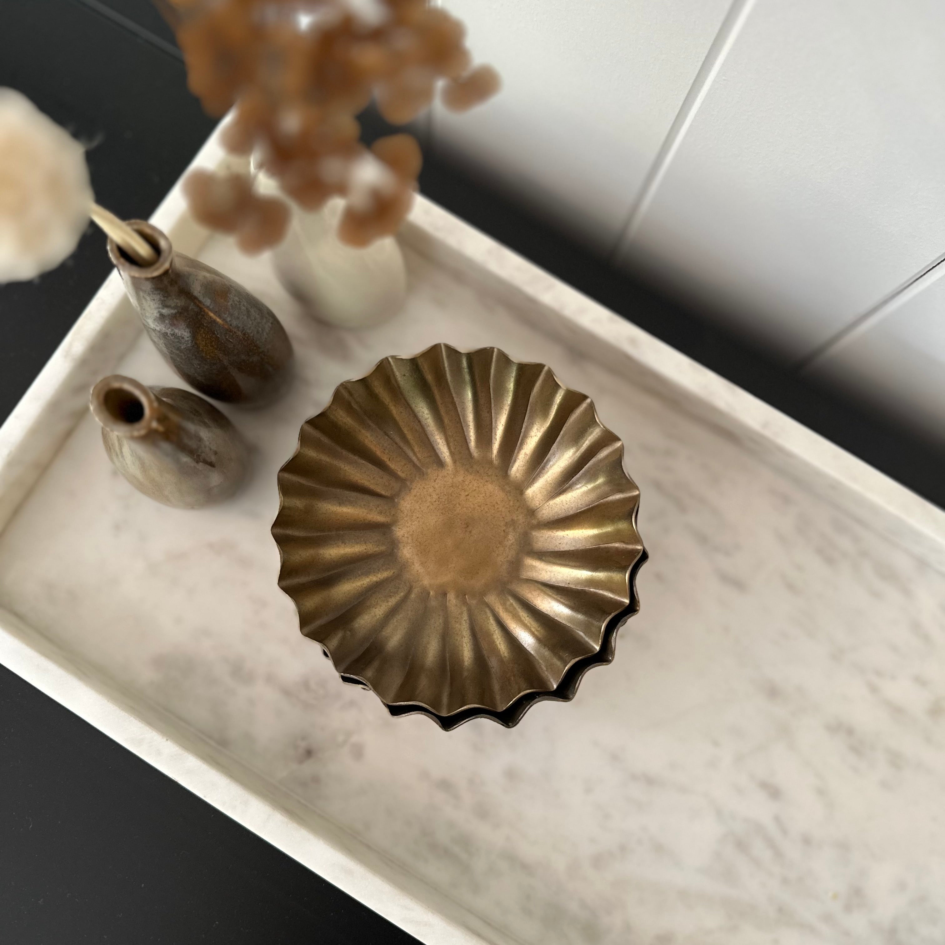 Decorative brass plate on a marble surface with vases and plants.