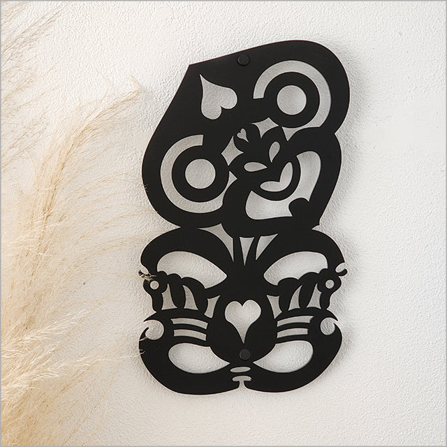 Decorative black Hei Tiki wall art with intricate patterns on a textured white background