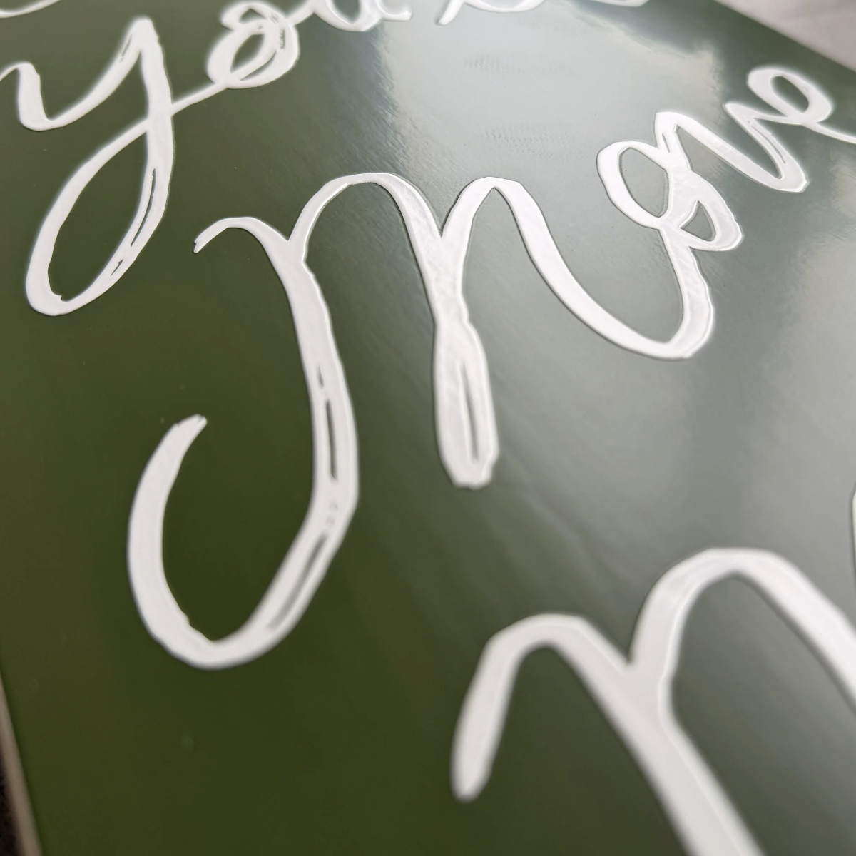 Close-up of a dark green sign with white cursive script lettering, showing part of the phrase 'you move'.