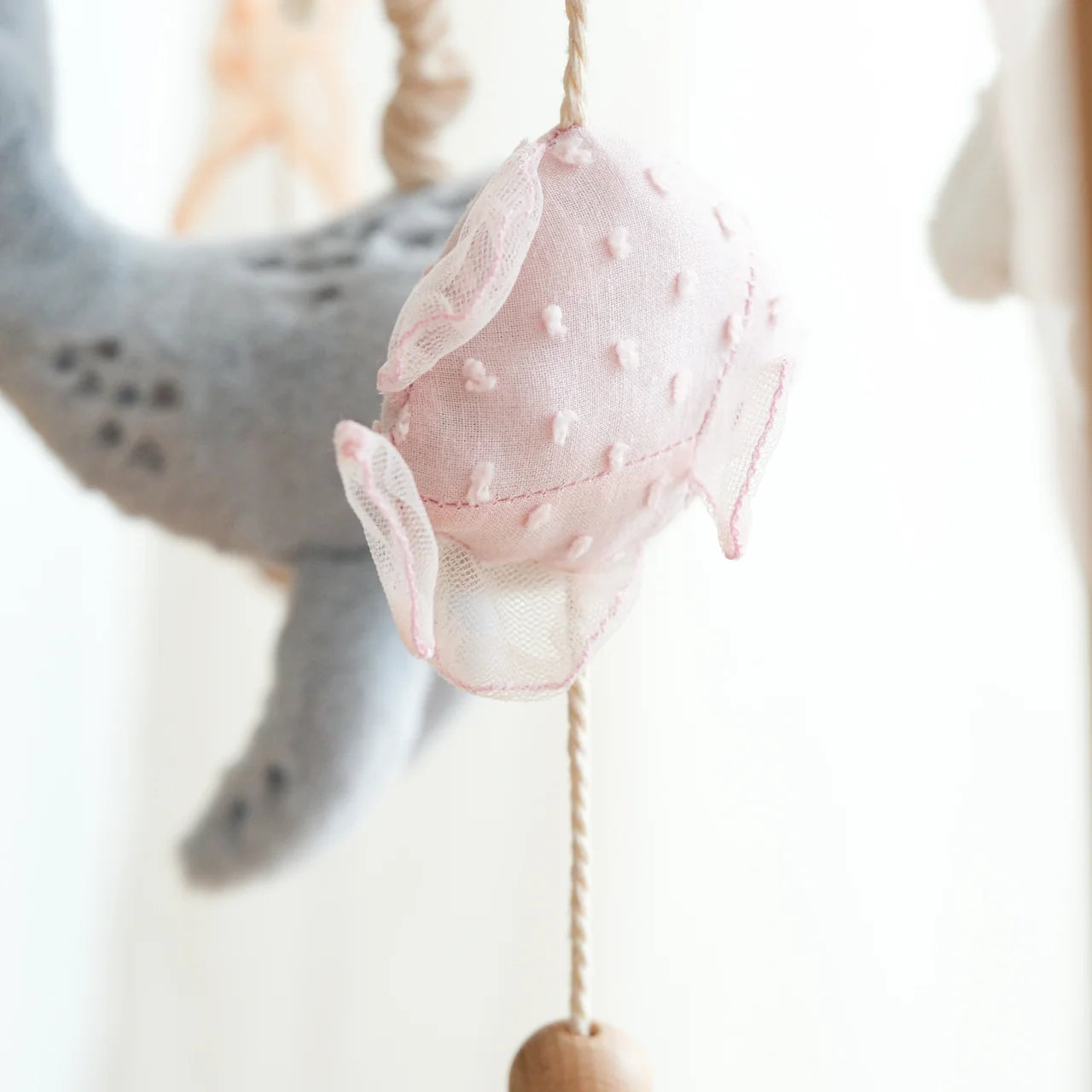 Pink shell-shaped decorative item hanging on a string with a blurred background