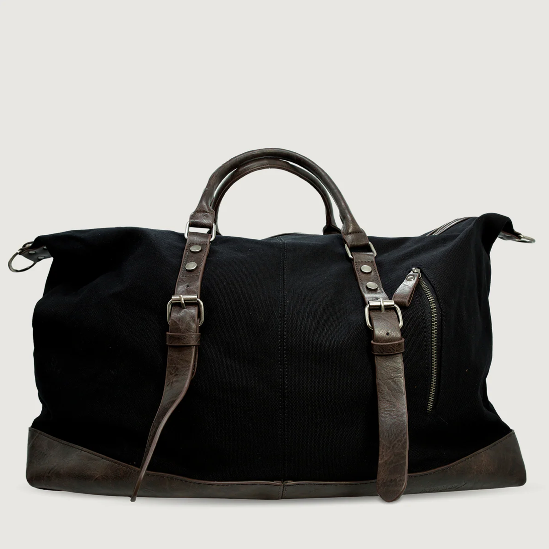 A black canvas duffel bag with dark brown leather handles, trim, and buckle straps, shown against a light gray background.