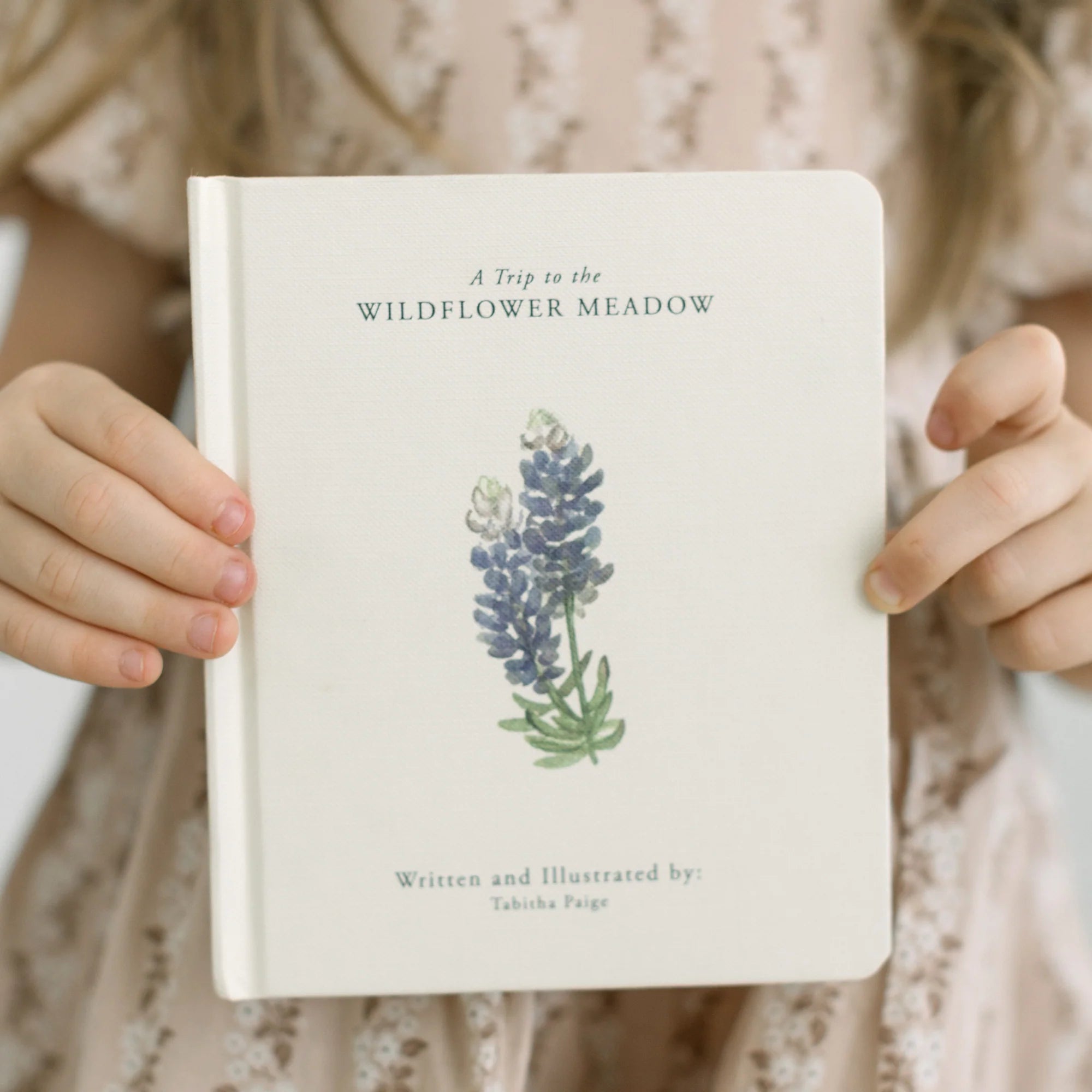 Book titled 'A Trip to the Wildflower Meadow' held by a person with floral clothing.