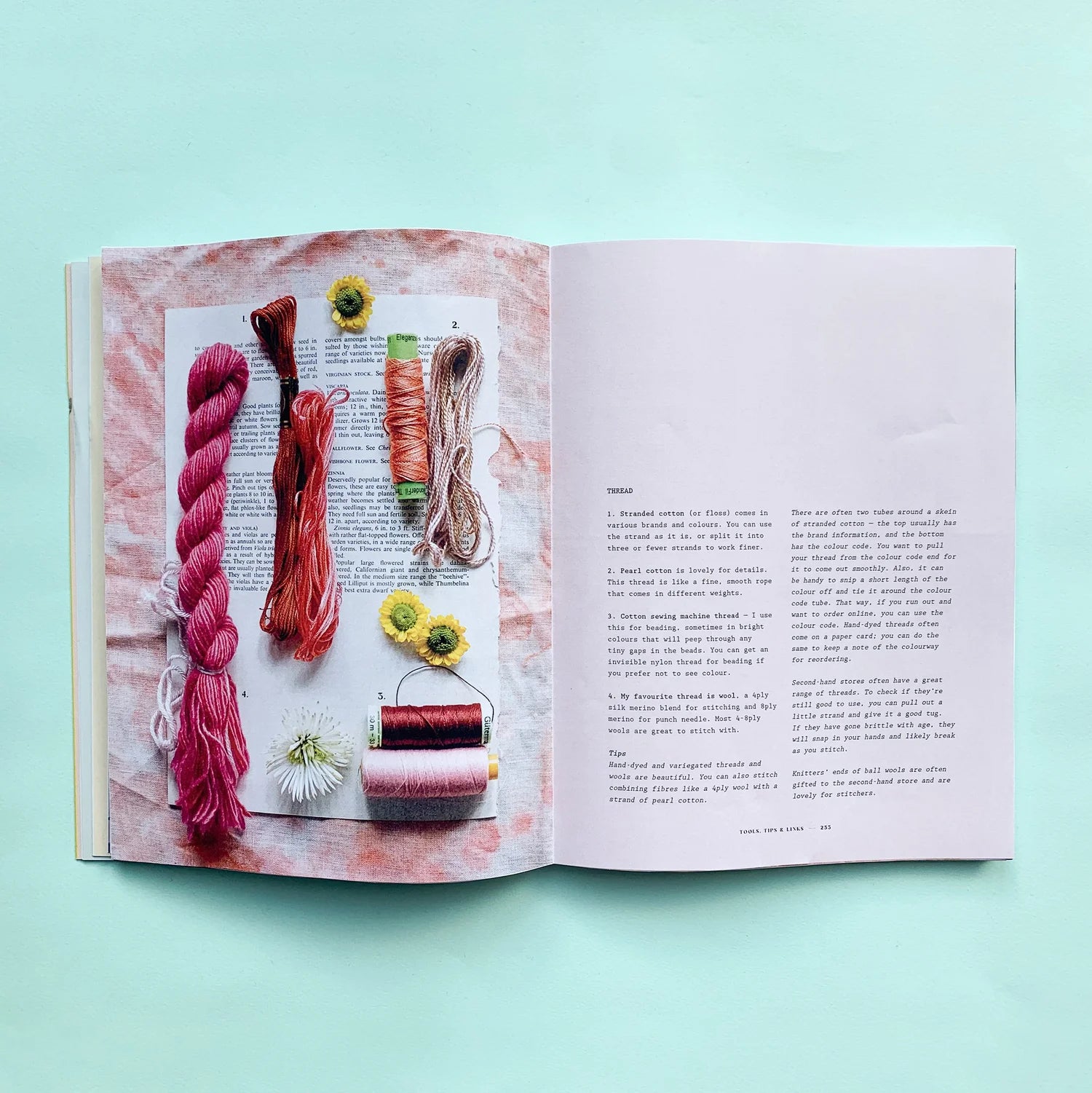 An open book laid flat on a mint green background, showing a knitting or crochet project page with text on the right and a collage of yarn skeins, thread, and small flowers on the left.