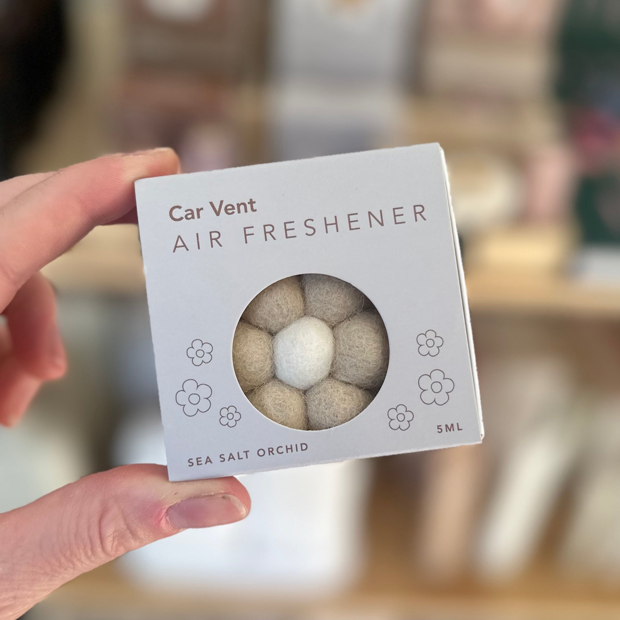 Hand holding a car vent air freshener packaging with a blurred background