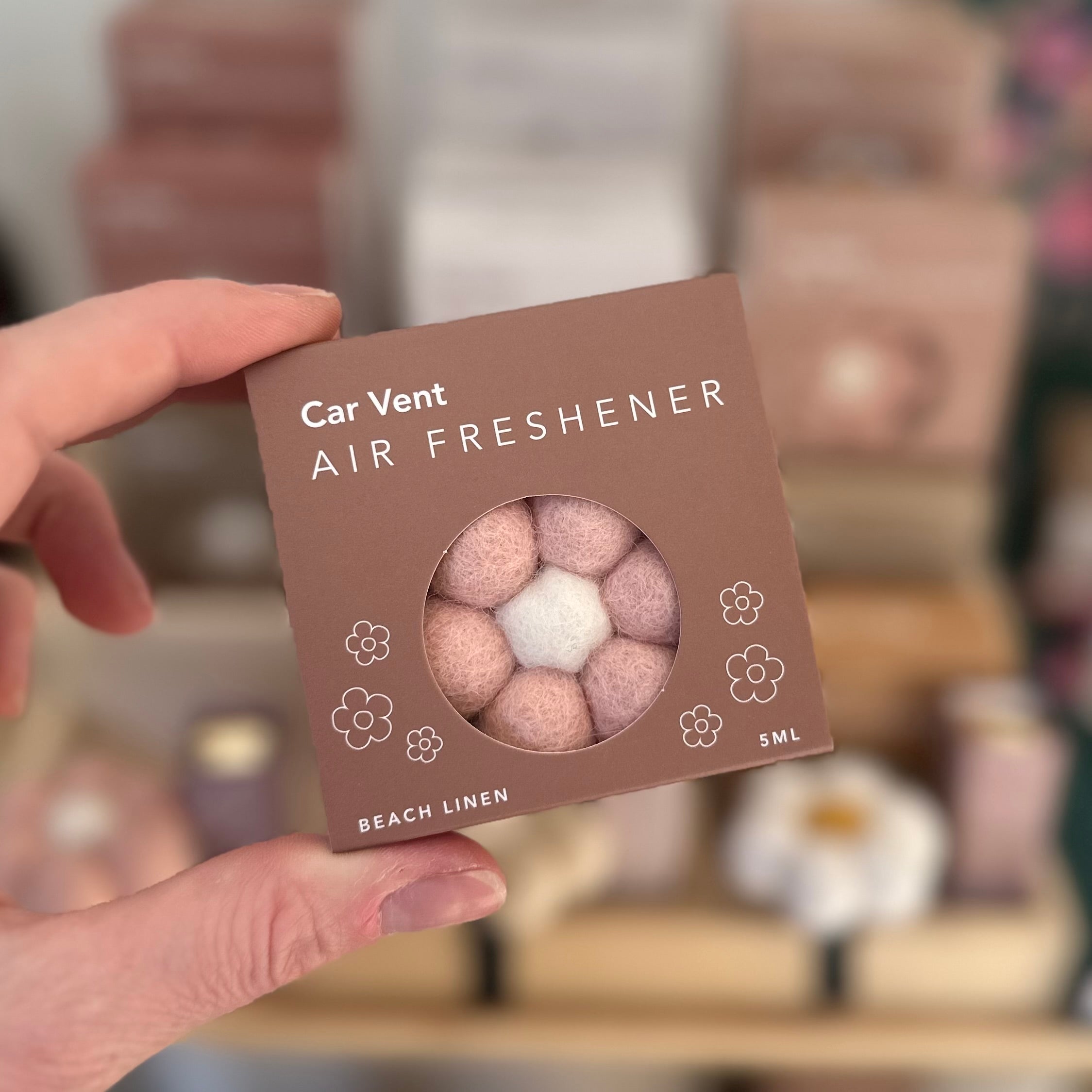 Hand holding a car vent air freshener packaging with 'Beach Linen' scent.