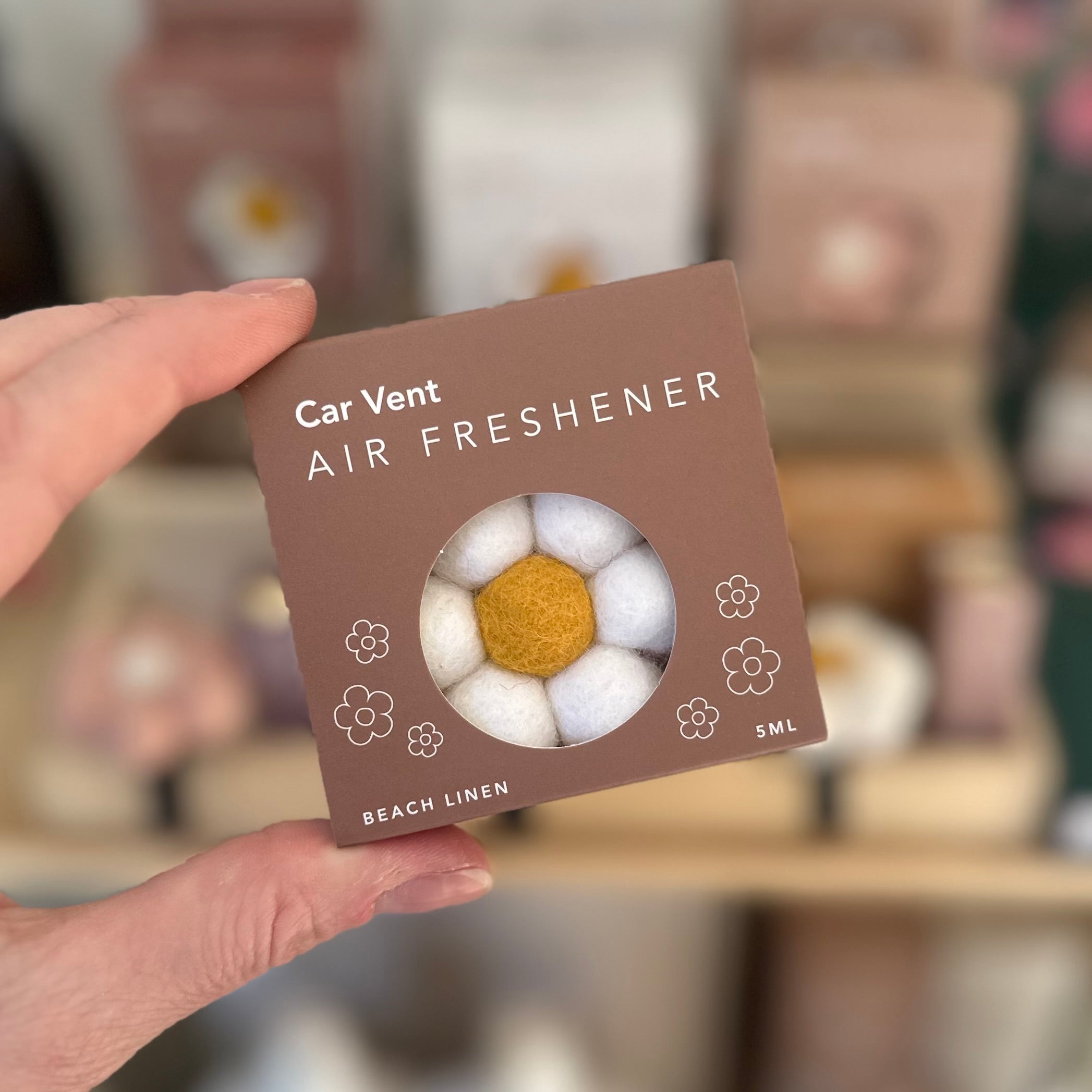 Car vent air freshener packaging with a hand holding it, blurred background
