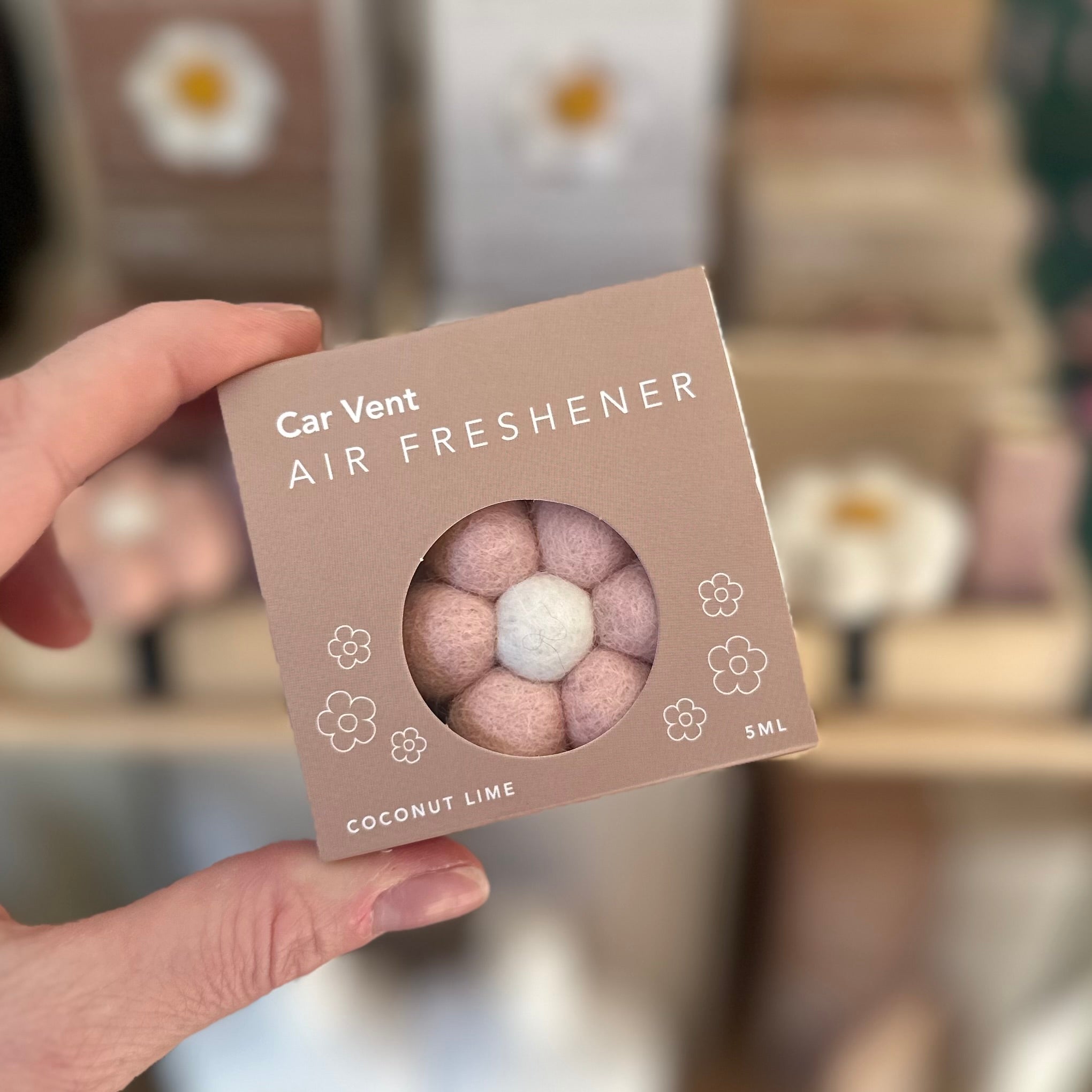 Car vent air freshener packaging held by a hand with a blurred background