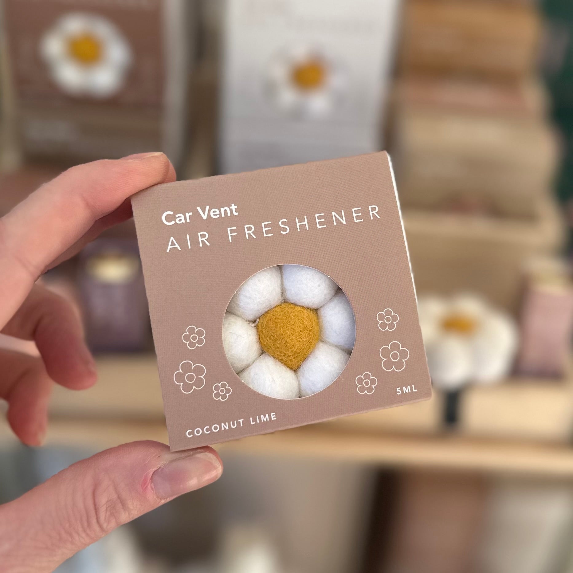 Car vent air freshener packaging with coconut lime scent held by a hand.