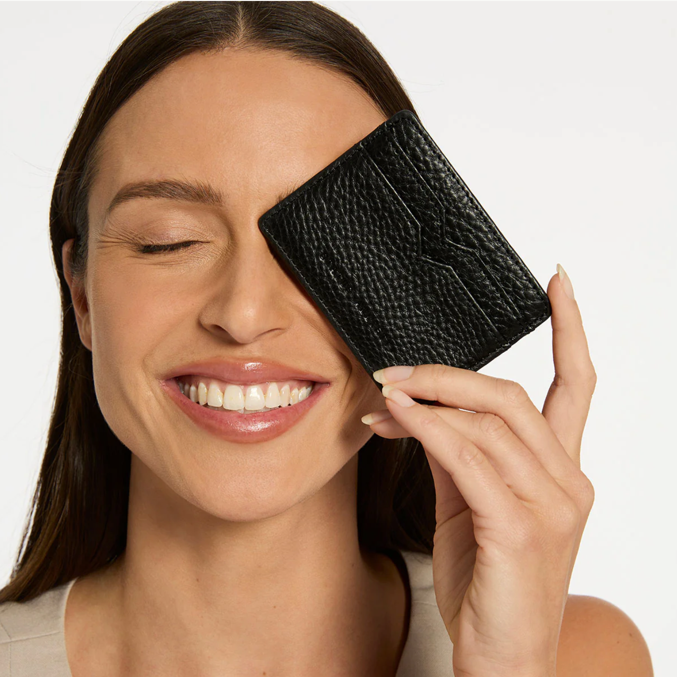 Woman holding a black textured wallet up to her face against a plain background