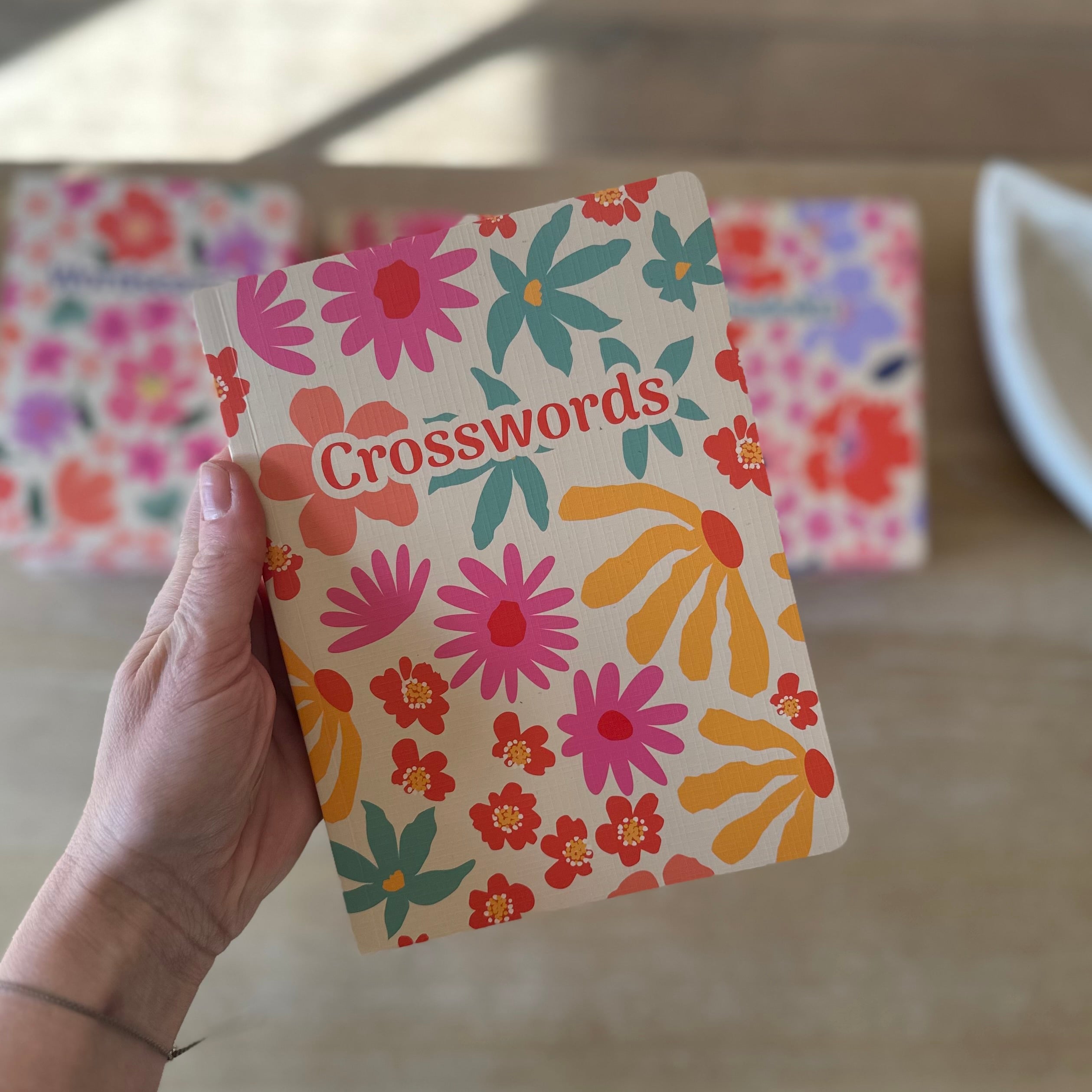 Floral notebook with 'Crosswords' text held by a hand on a blurred background